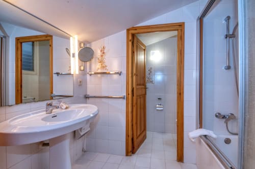 Modern bathroom in Calella apartment with white tiles, wooden-framed mirror, sink, and shower enclosure at Finques Garcia