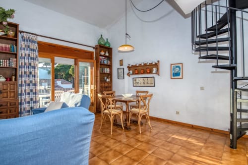 Bright apartment living room in Palafrugell with blue sofa, dining table, wooden furnishings, and sea view through glass