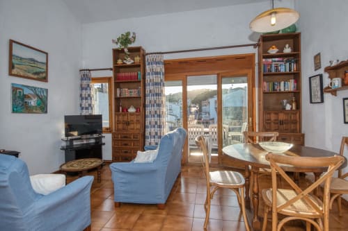 Bright apartment living room in Calella, Palafrugell with blue chairs, wooden dining table, TV, and balcony with city views