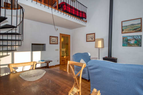Bright apartment living room in Calella with blue sofa, wooden table, spiral staircase, and framed artwork on white walls