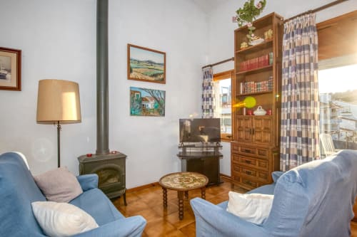 Cozy apartment living room in Palafrugell with blue armchairs, fireplace, wooden bookcase, and city views