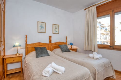 Bright bedroom with twin beds, wooden headboard, and city view in Calella apartment