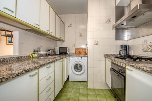 Modern kitchen in Calella apartment with cream cabinets, granite counters, stainless appliances, and washer