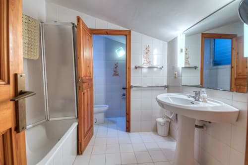 Spacious bathroom in Calella apartment with pedestal sink, bathtub, shower, and wooden doors