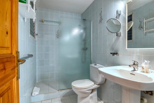 Modern bathroom with glass shower, white sink, toilet, and mirror in Calella apartment center