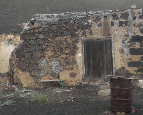 Rustic stone building at Finca de La Geria in Yaiza with weathered walls, wooden door, and rusty barrel