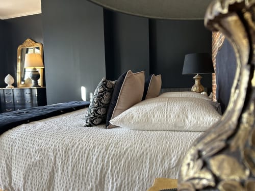 Chambre élégante au Clos Mahiel avec literie blanche, coussins décoratifs, murs foncés, miroir doré et lampes majestueuses . Chambre Inès-Style.