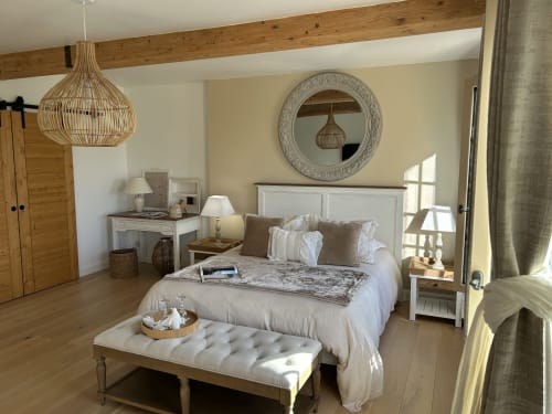 Chambre lumineuse et subtile au Clos Mahiel avec poutres apparentes, lit blanc, lin, parquet naturel, suspension tissée et tons neutres chaleureux. Chambre Aurore-Lin.