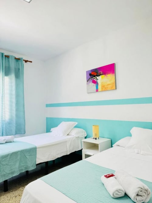 Habitación moderna en Apartamentos Rocamar con camas individuales, detalles turquesas y obras de arte abstracto coloridas