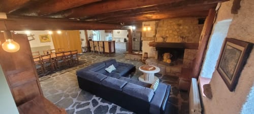 Salon rustique d'Au Bord de la Dunière avec cheminée, canapé sombre et coin repas