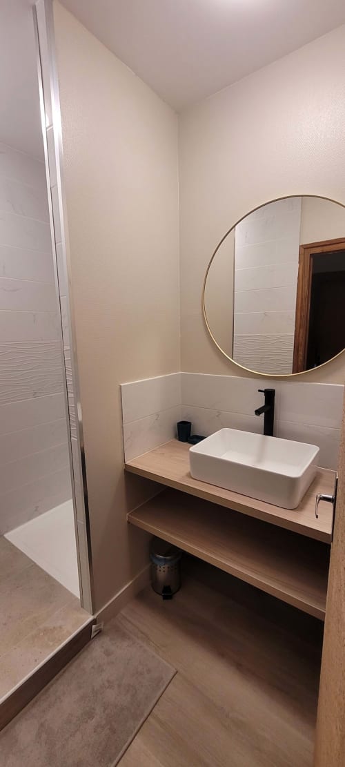 Salle de bain moderne du gîte Au Bord de la Dunière avec lavabo blanc, robinetterie noire, miroir rond et douche