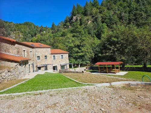 Petite maison en pierre à Au Bord de la Dunière à Sainte Sigolène, pelouse verte, forêt en arrière-plan et abri aux tuiles rouges
