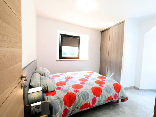 Chambre de cottage moderne à Au Bord de la Dunière avec vue sur la rivière, literie rouge éclatante et mobilier en bois