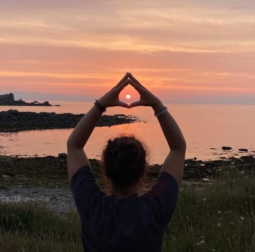 Person making heart shape with hands framing sunset over ocean at Espace Ker Gana, Plourin