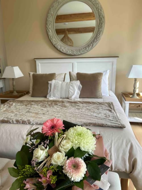 Chambre raffinée et élégante au Clos Mahiel avec tête de lit blanche, fleurs fraîches, miroir orné et décoration sobre. Chambre Aurore-Lin.