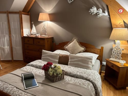Chambre cosy sous les toits au Clos Mahiel avec poutres apparentes, parures de draps blancs et taupe, meubles anciens et fleurs fraîches à Saint-Romain-de-Colbosc France