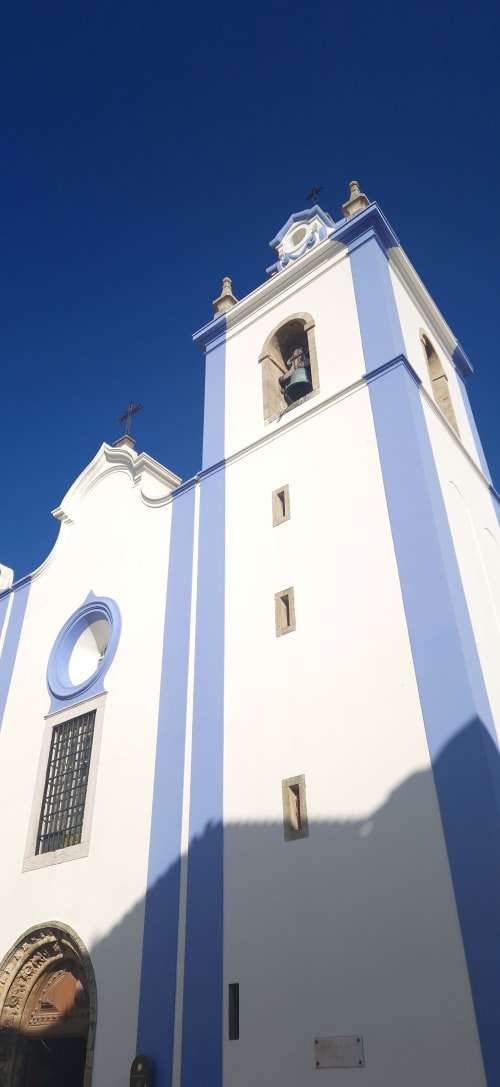 Igreja portuguesa branca e azul com alto campanário contra céu limpo em Venda do Pinheiro