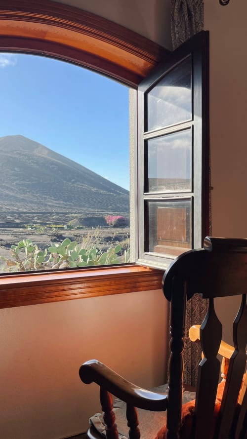 Vista desde la ventana abierta de la habitación del hotel Finca de La Geria hacia el paisaje de montaña volcánica en Yaiza