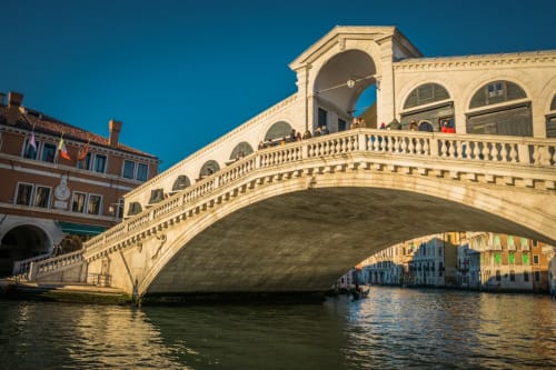 Rialto Bridge spanning Grand Canal in Venice with colorful buildings and gondolas reflected in water under clear blue sky