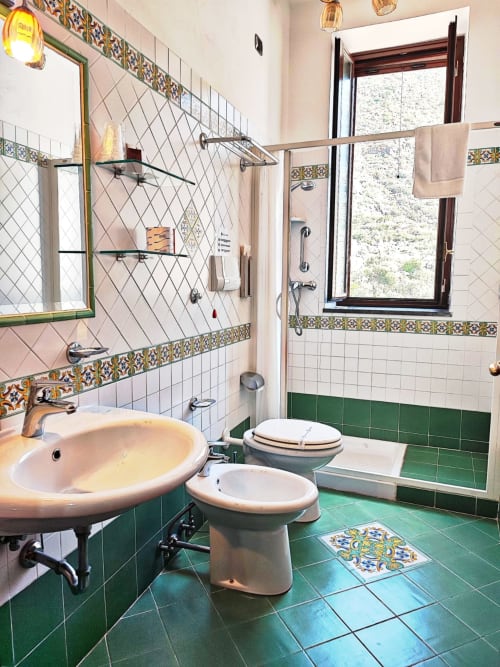 Bagno vintage colorato all'Hotel Principe di Rinella con piastrelle verdi, lavabo bianco, bidet e dettagli ceramici decorativi