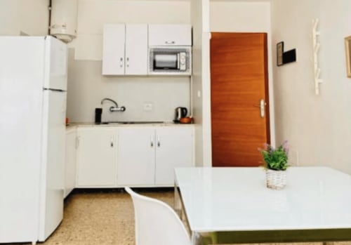 Kitchenette compacta con muebles blancos, microondas de acero inoxidable y puerta de madera en Apartamentos Rocamar, Santa Cruz de la Palma