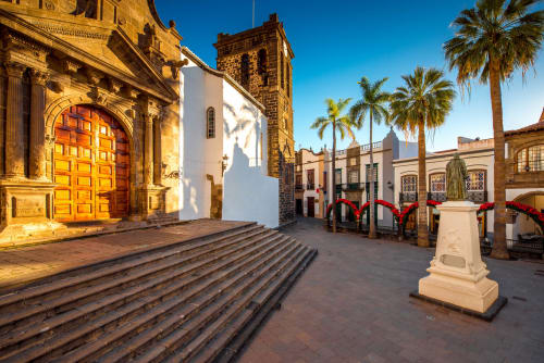 Plaza colonial en Santa Cruz de la Palma con iglesia de piedra dorada, puertas rojas, palmeras y decoraciones festivas navideñas