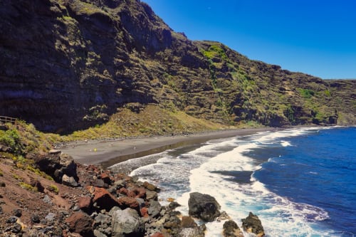 Cala de arena negra con acantilados imponentes y olas del océano en Santa Cruz de la Palma, Islas Canarias