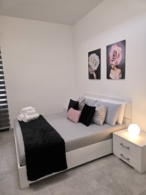 Camera moderna a Raymihome Torino con letto bianco, opera d'arte rosa decorativa, corridoio nero e palette di colori neutri