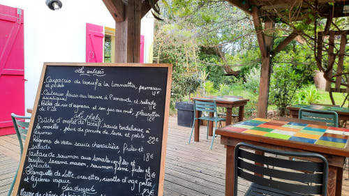 Espace de restauration extérieure à Loc'Maria Belle Île avec tableau de menu, tables colorées et jardin