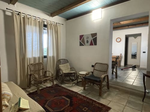 Bright cottage living room with rattan chairs, sea view windows, and rustic wood ceiling in Orosei villa