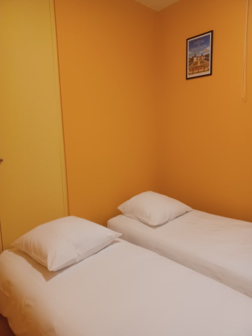 Deux lits blancs avec oreillers dans une chambre orange vif de l'Hôtel Accolade Châteaudun, avec une œuvre d'art de château au mur