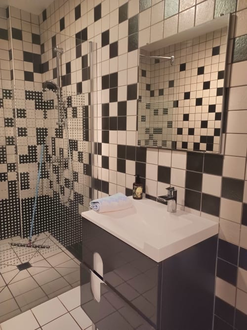 Salle de bains moderne aux carreaux noirs et blancs de l'hôtel Accolade Châteaudun avec douche, lavabo et carrelage décoratif