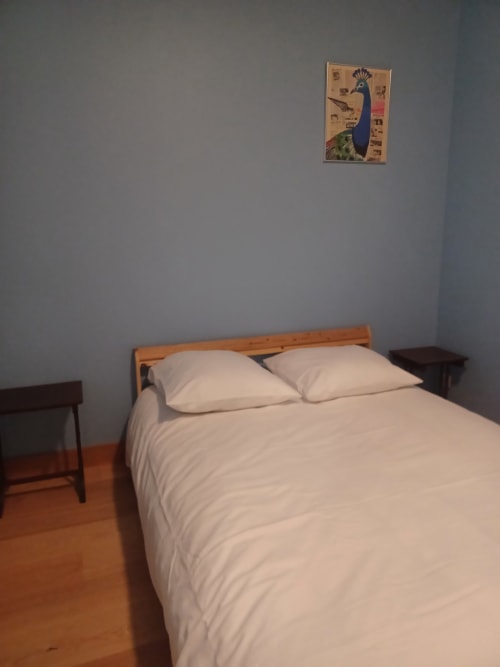 Chambre de l'hôtel Accolade à Châteaudun avec lit en bois, linge blanc et décoration de paon au mur