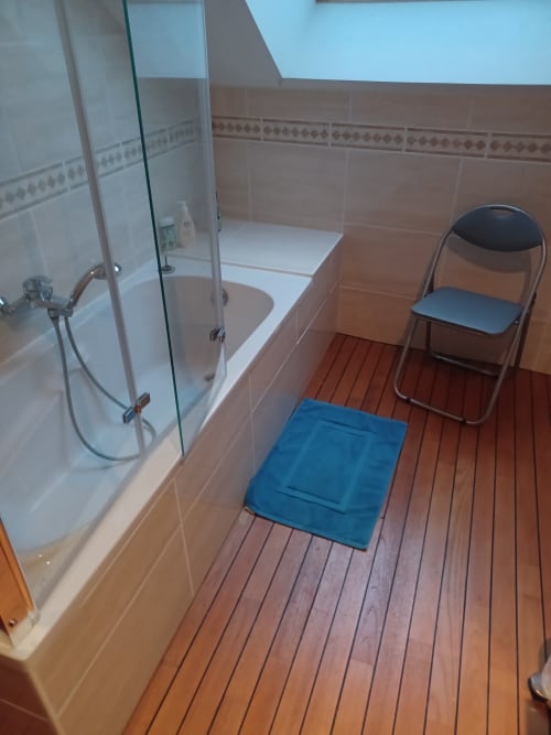 Hall de réception de l'hôtel Accolade avec cabine de douche en verre, tapis de bain bleu, fauteuil et parquet