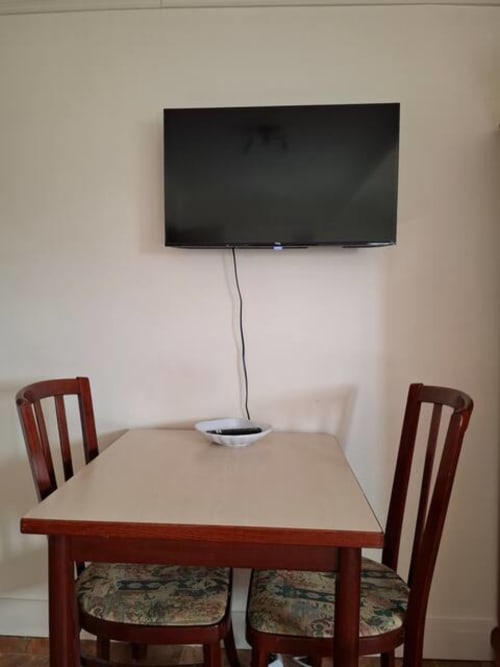 Coin salle à manger de l'appartement Accolade avec TV murale, table et chaises en bois à Châteaudun