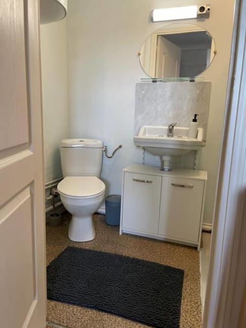 Salle de bain compacte de l'appartement Accolade à Châteaudun, équipée de toilettes, lavabo sur colonne, miroir et rangements blancs.