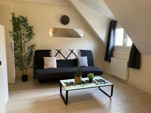Appartement mansardé moderne à Accolade Châteaudun avec canapé noir, table basse blanche et vue sur la ville