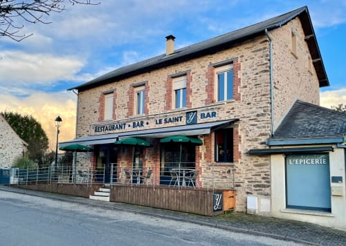 Façade en pierre du restaurant Le Saint Bar à Saint Ybard, France, avec store vert