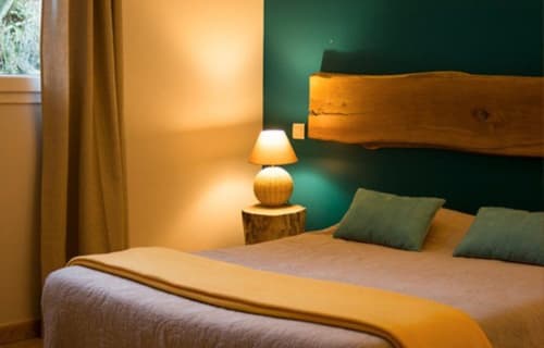 Chambre accueillante à Vista D'oro à Monacia d'Aullène avec éclairage chaleureux, lit en bois, mur vert et vue sur la mer