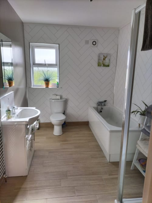 Modern bathroom at Ballymultimber Cottages with white herringbone tiles, wooden flooring, sink, toilet, and bathtub with