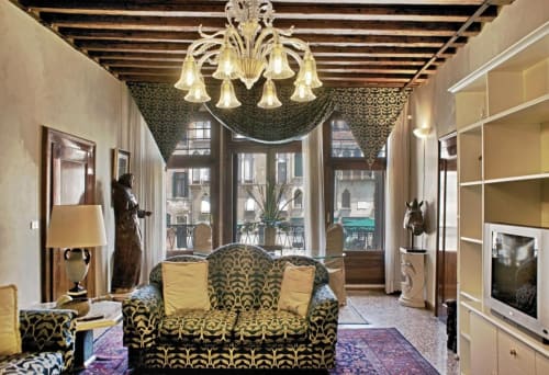Lussuoso soggiorno di palazzo veneziano con divano decorato, lampadario, finestre con vista sul mare e arredamento elegante