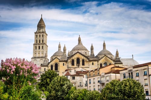Cathédrale romane à dôme doré et clocher surplombant La Douze, France, avec fleurs roses en fleur