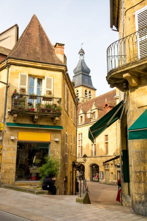 Charming medieval street in La Douze with golden stone buildings, a turret, and church tower in the background