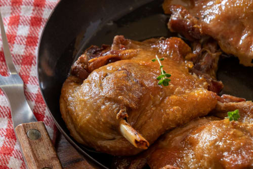 Braised chicken thighs in rich brown sauce, garnished with thyme, served in a cast iron skillet at Domaine de la Grande