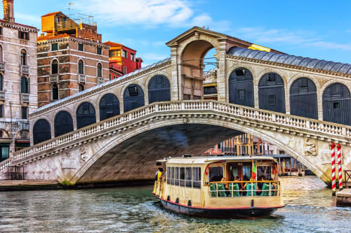 Yellow vaporetto boat under Rialto Bridge with historic Venice buildings and canal water