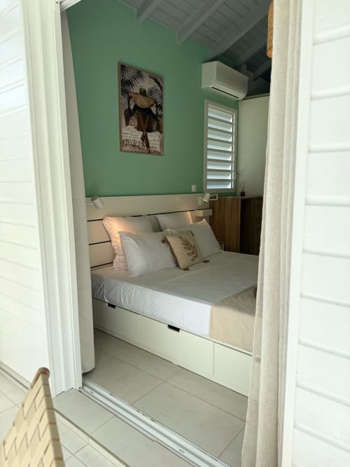 Chambre du bungalow Alpinia à Domaine de la Glacière avec murs verts, lit blanc et décoration tropicale