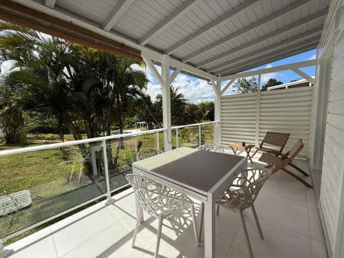 Terrasse couverte du bungalow Alpinia, Domaine de la Glacière, avec table à manger, chaises et vue sur le jardin tropical à Petit