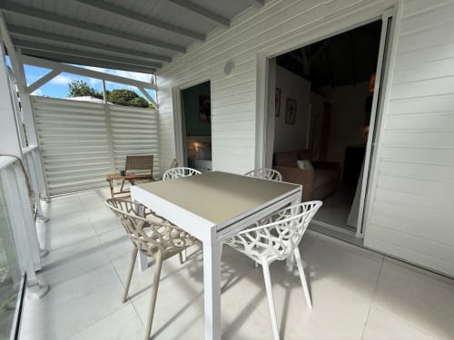Terrasse du bungalow Alpinia à la Domaine de la Glacière avec table à manger, chaises blanches et portes vitrées ouvertes