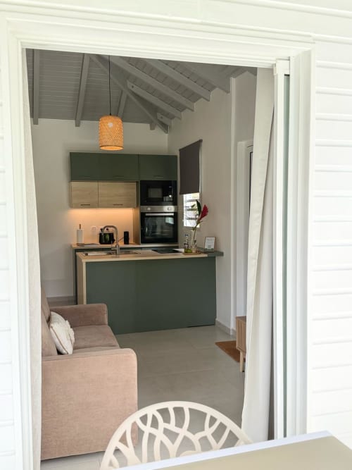 Cuisine du bungalow Alpinia au Domaine de la Glacière à Petit Bourg, avec mobilier vert, électroménagers modernes et espace détente.