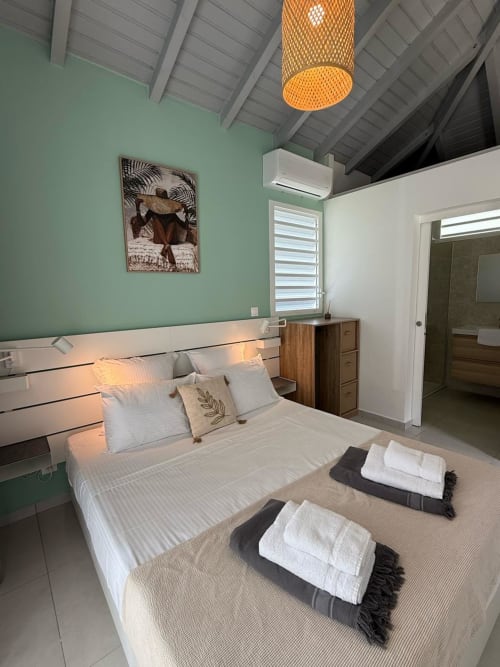 Chambre de la Bungalow Alpinia au Domaine de la Glacière avec murs vert menthe, literie blanche et luminaire orange